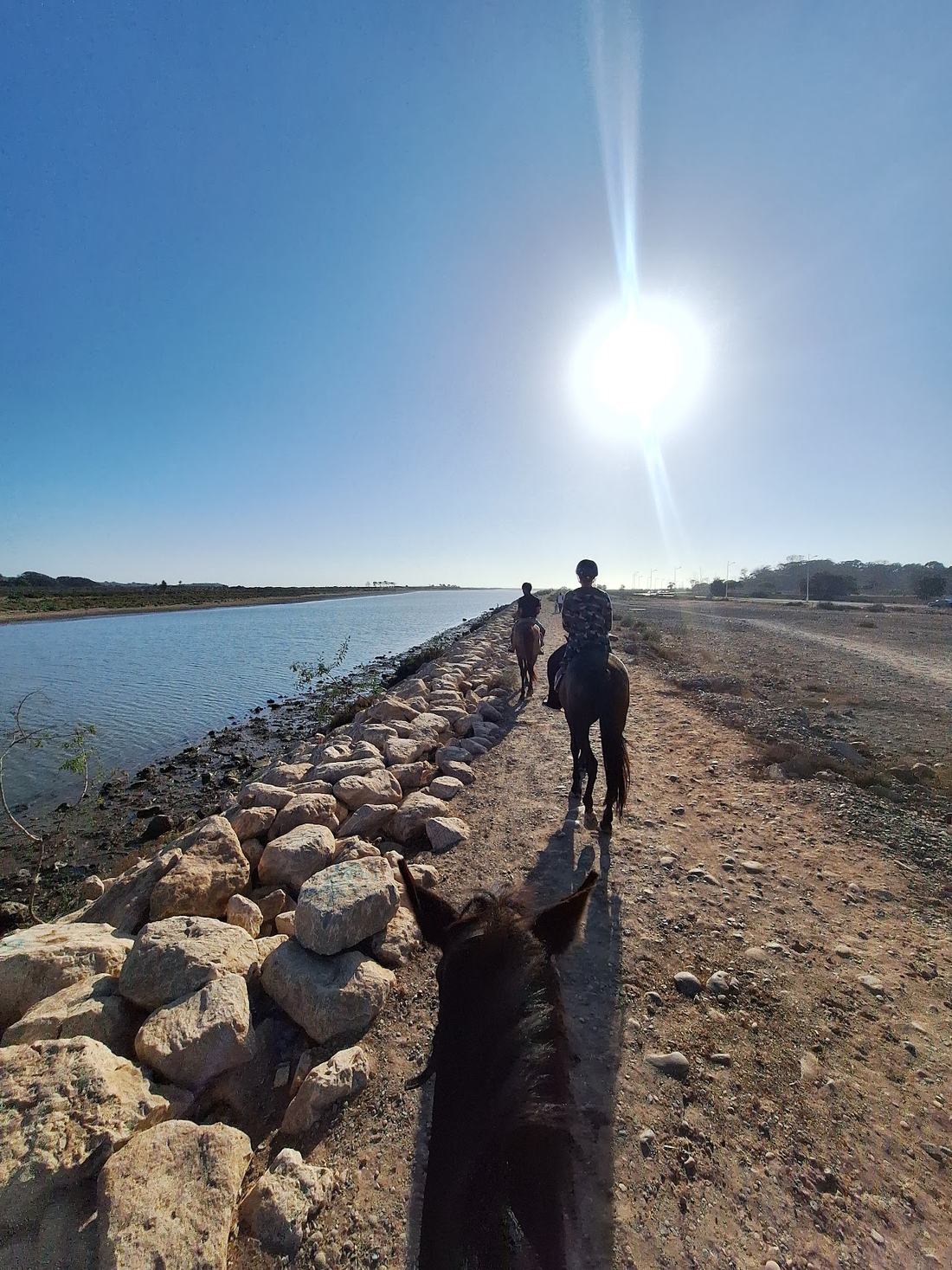 Rider on horseback heading into the sun along the riverside causeway near Agadir